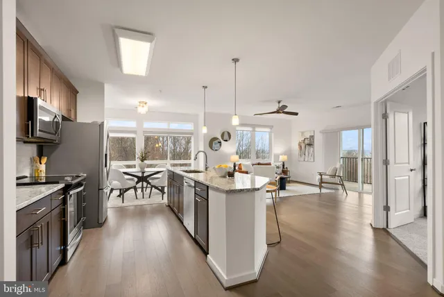 a kitchen with stainless steel appliances granite countertop a stove top oven a sink a dining table and chairs with wooden floor