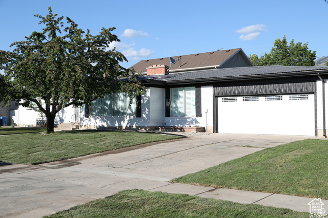 702 North 100 West Logan, UT 84321 - Photo 1 of 58 View of front of house featuring driveway, an attached garage, brick siding, a front lawn, and metal roof