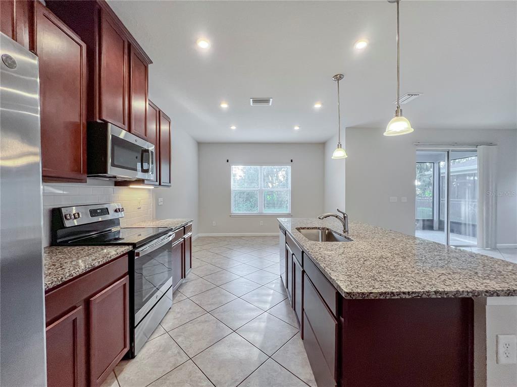 8511 Rain Lily Crossing Parrish, FL 34219 - Photo 7 of 34 a kitchen with granite countertop kitchen island stainless steel appliances a sink stove and cabinets