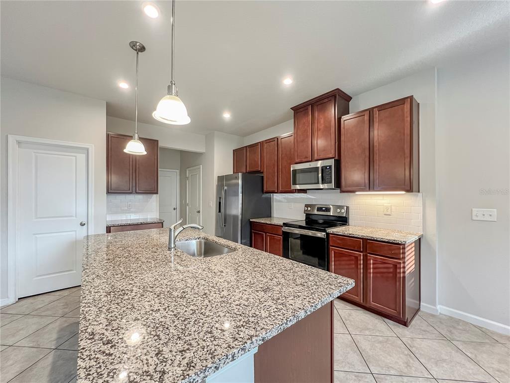 8511 Rain Lily Crossing Parrish, FL 34219 - Photo 8 of 34 a kitchen with kitchen island granite countertop wooden cabinets a stove a oven and a refrigerator with wooden floor
