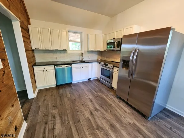 a kitchen with granite countertop a refrigerator a sink dishwasher a stove and white countertops with wooden floor