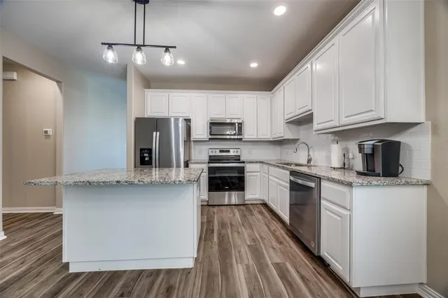 a kitchen with stainless steel appliances granite countertop a refrigerator a stove top oven a sink and dishwasher with wooden floor