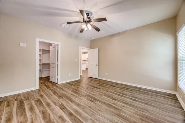 a view of an empty room with wooden floor and a ceiling fan