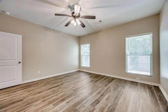 an empty room with wooden floor chandelier fan and windows