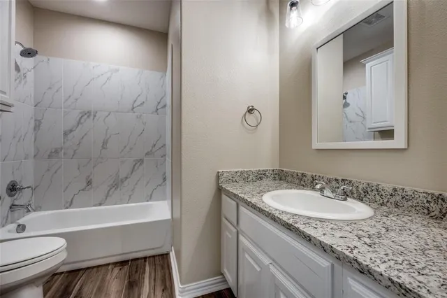 a bathroom with a granite countertop sink a toilet a mirror and bathtub