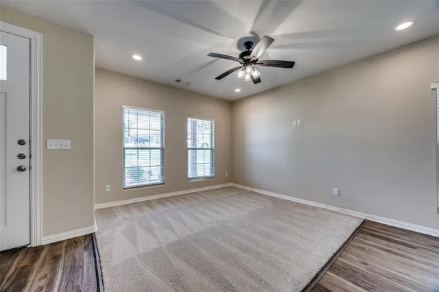 an empty room with wooden floor fan and windows