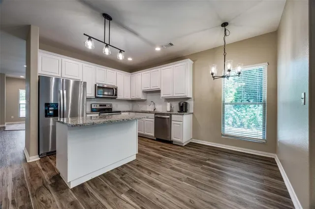 a kitchen with stainless steel appliances granite countertop a refrigerator a sink dishwasher a stove and white countertops with wooden floor