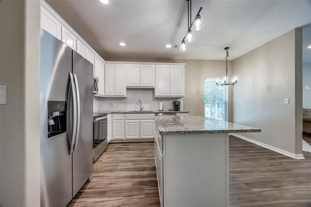 a kitchen with granite countertop a refrigerator a sink and white cabinets