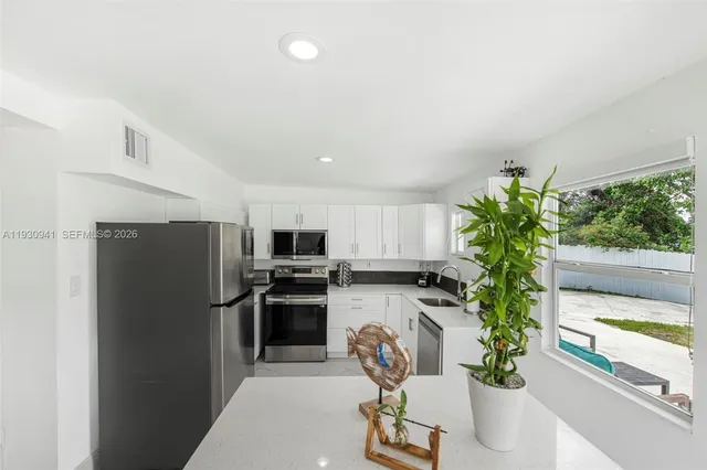 a kitchen with a potted plant a refrigerator and a view of living room