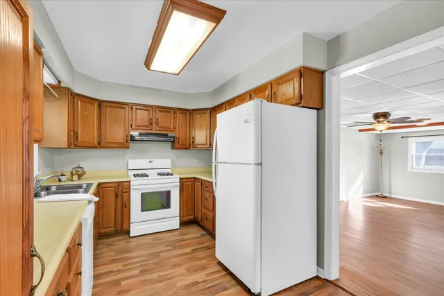 a kitchen with stainless steel appliances a refrigerator a sink a stove and white cabinets with wooden floor
