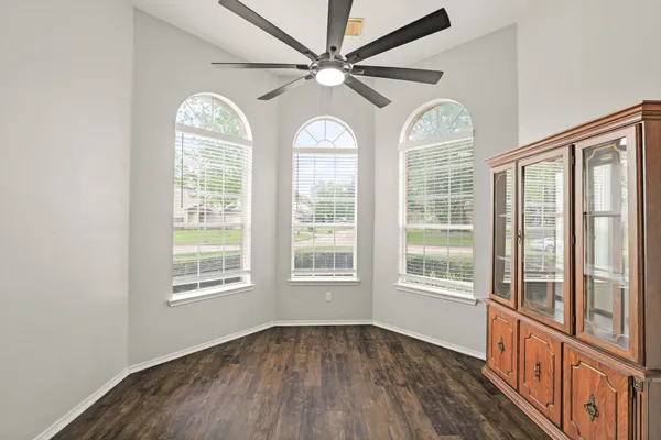 an empty room with wooden floor fan and windows