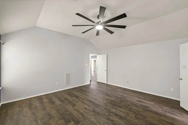 a view of an empty room with wooden floor and a ceiling fan