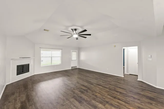 an empty room with wooden floor fireplace and windows