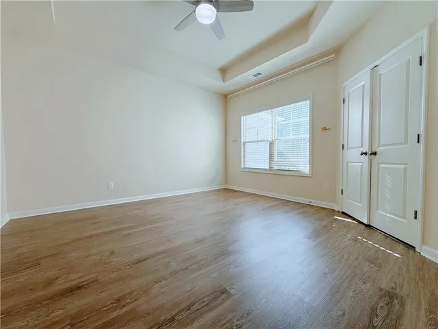 an empty room with wooden floor chandelier fan and windows