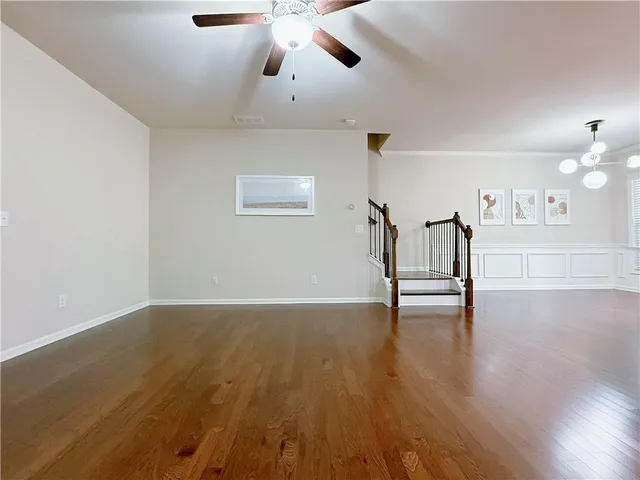 a view of an empty room with wooden floor and a ceiling fan