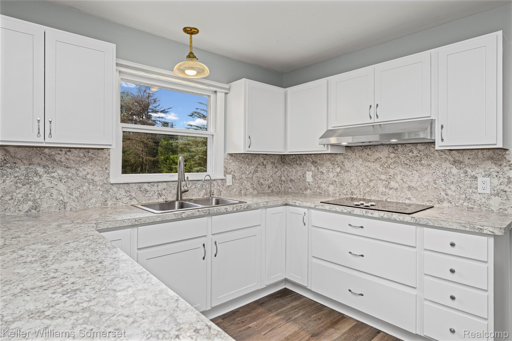 2344 Rochester Road Leonard, MI 48367 - Photo 19 of 66 Bright kitchen featuring white shaker cabinetry, patterned countertops and backsplash, stainless steel double basin sink, and a built-in cooktop with an overhead range hood