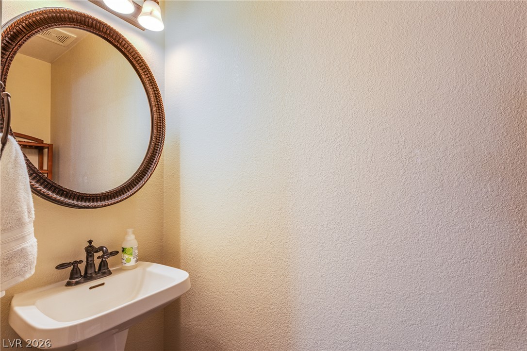 253 Camelback Ridge Avenue Henderson, NV 89012 - Photo 8 of 26 A classic pedestal sink sits beneath a decorative round mirror in this charming powder room.