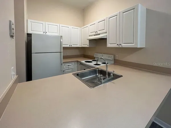 a kitchen with stainless steel appliances granite countertop a refrigerator a stove a sink and white cabinets