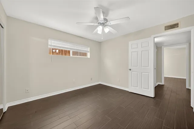 an empty room with wooden floor fan and windows