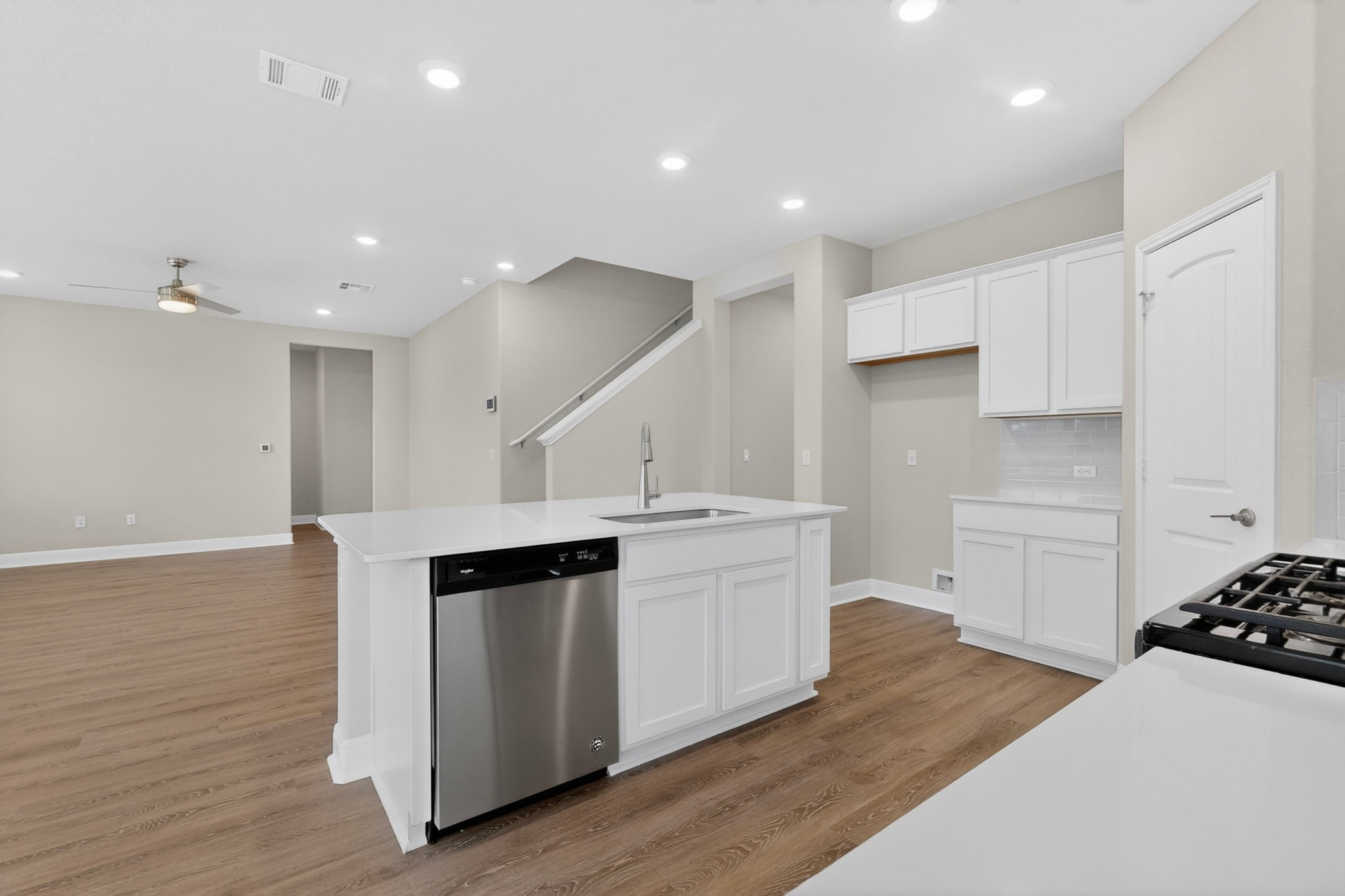 16809 Guido Cove Pflugerville, TX 78660 - Photo 12 of 40 Modern kitchen featuring a central island with an integrated stainless steel dishwasher and sink, white cabinetry, a light-colored countertop, and a white subway tile backsplash