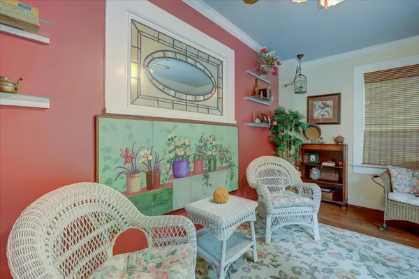 a view of small white house with large trees and flower plants