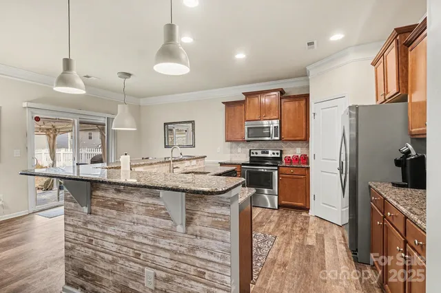 a kitchen with stainless steel appliances granite countertop a refrigerator a stove a sink a dining table and chairs with wooden floor