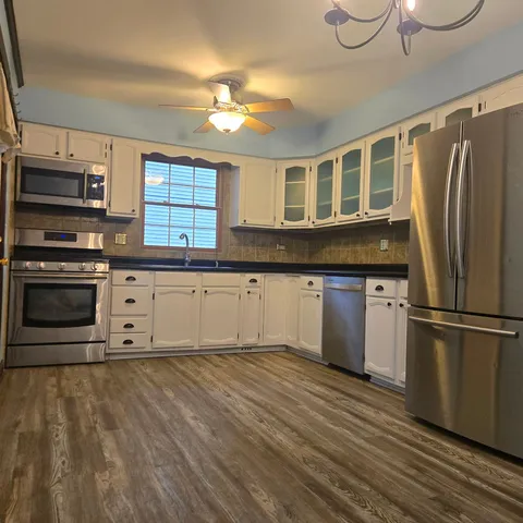 a kitchen with stainless steel appliances granite countertop a refrigerator a stove a sink and dishwasher with wooden floor