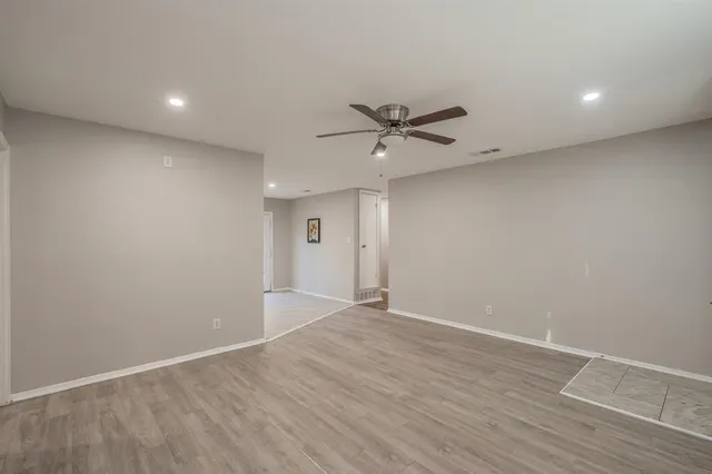 a view of an empty room with wooden floor and a ceiling fan
