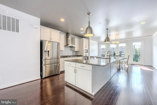 a kitchen with stainless steel appliances a refrigerator a sink dishwasher a oven and a dining table with wooden floor