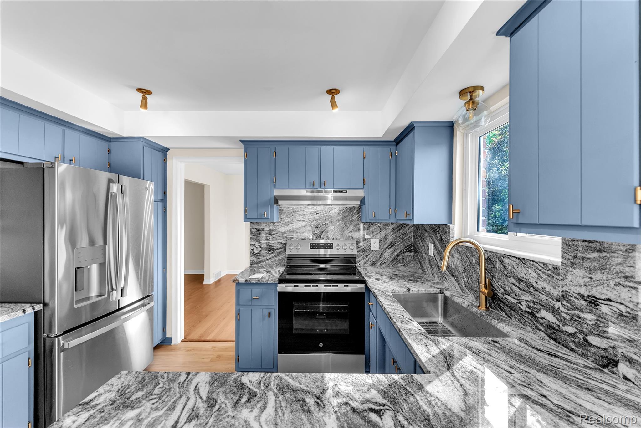 54011 Mound Road Utica, MI 48316 - Photo 8 of 27 Kitchen featuring blue cabinets, stainless steel appliances, decorative backsplash, light wood-style flooring, and under cabinet range hood