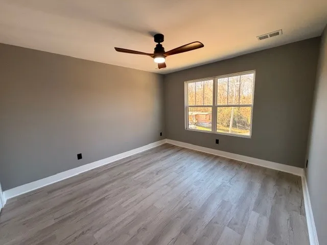 an empty room with wooden floor ceiling fan and windows