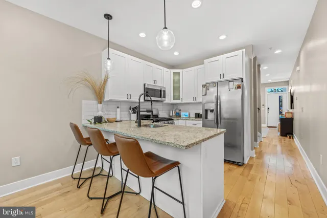 a kitchen with stainless steel appliances granite countertop a refrigerator a sink dishwasher a stove and a dining table with wooden floor