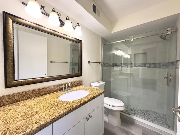 a bathroom with a granite countertop sink toilet a mirror and shower
