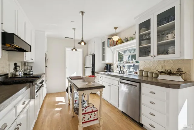 a kitchen with stainless steel appliances granite countertop a sink stove and white cabinets with wooden floor