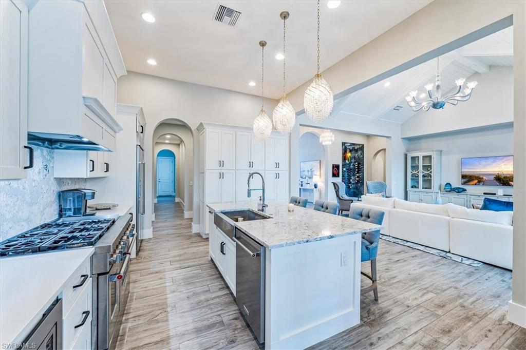 3181 Cullowee Lane Naples, FL 34114 - Photo 13 of 43 a large kitchen with stainless steel appliances a stove a sink dishwasher and a dining table with wooden floor