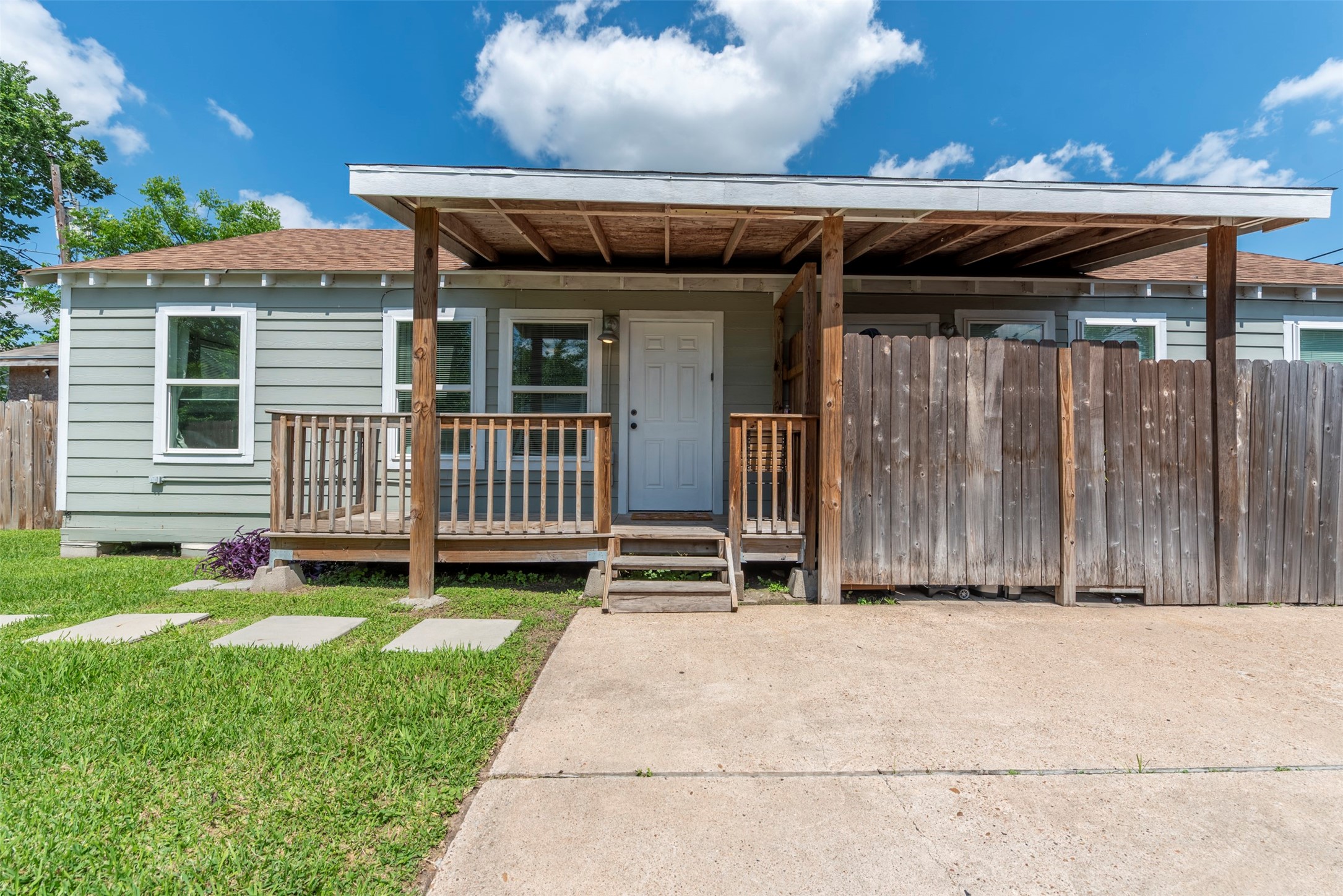 1121 Panama Street Houston, TX 77009 - Photo 35 of 35 Front exterior with sage-green lap siding, white trim, covered front porch with exposed wood beam ceiling, wood railing, pendant wall light, and concrete driveway.