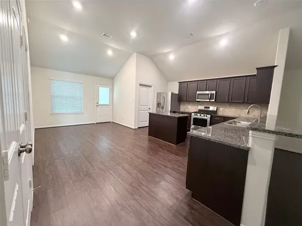 a kitchen with stainless steel appliances granite countertop a refrigerator a stove top oven a sink and dishwasher with wooden floor