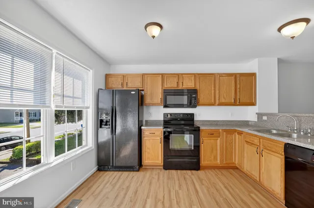 a kitchen with stainless steel appliances granite countertop a refrigerator a stove top oven and a sink with wooden floors