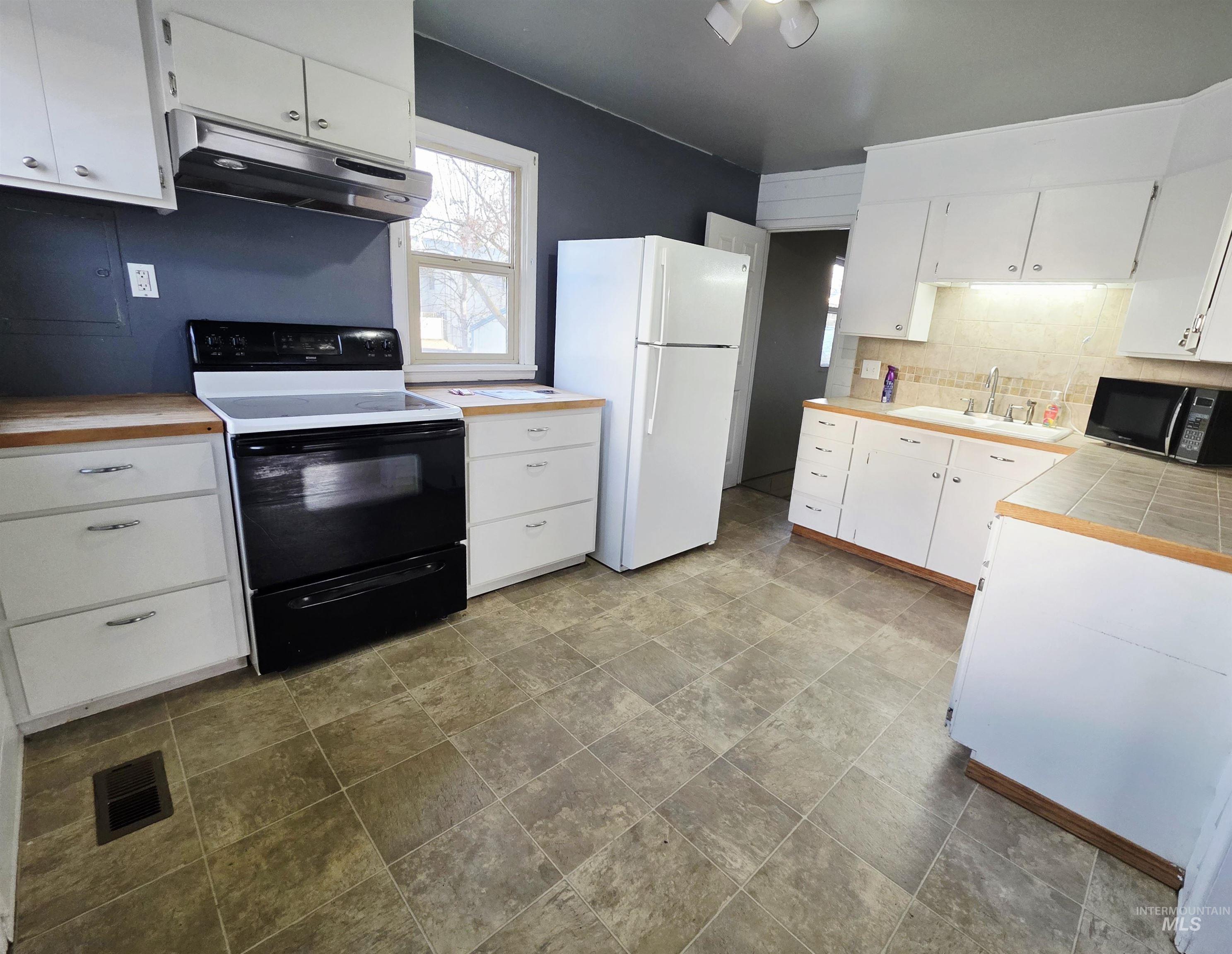 2127 12th Avenue Lewiston, ID 83501 - Photo 8 of 27 Kitchen featuring white cabinetry, black appliances, decorative backsplash, and stone finish floors