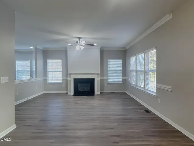 an empty room with wooden floor fireplace and windows