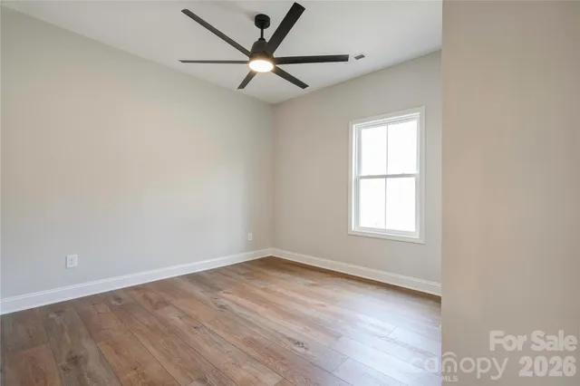 an empty room with wooden floor ceiling fan and windows