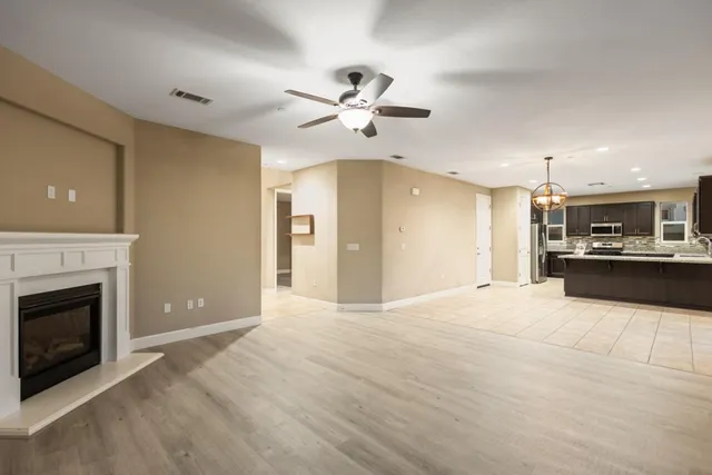 a view of an empty room with kitchen and fireplace