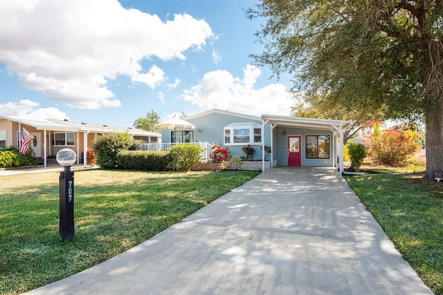 a view of a white house with a yard plants and large tree