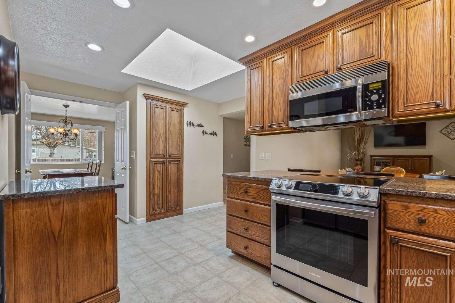 8720 Cornwall Drive Boise, ID 83704 - Photo 8 of 24 Kitchen featuring appliances with stainless steel finishes, brown cabinets, dark stone countertops, recessed lighting, and a textured ceiling