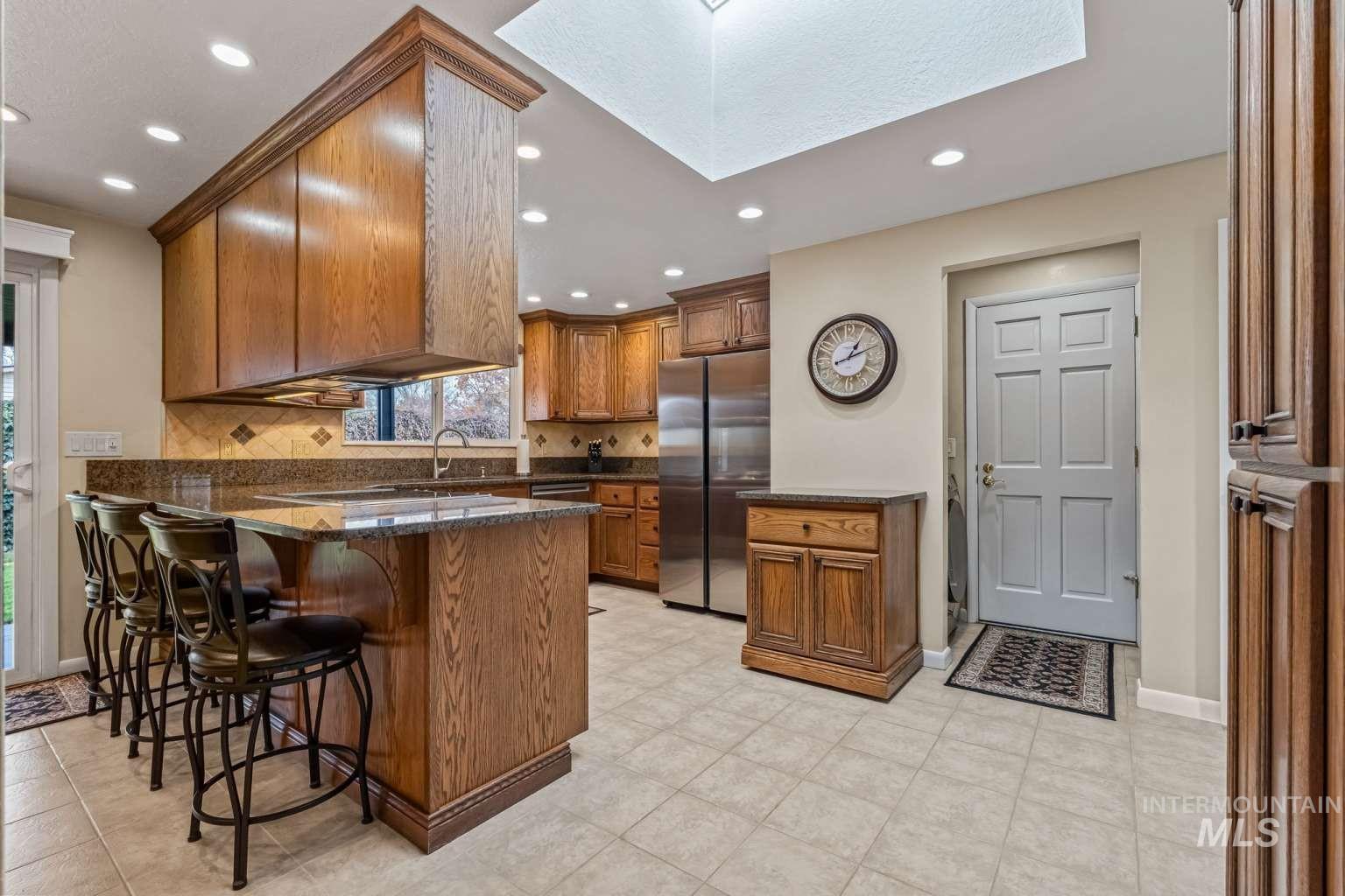 8720 Cornwall Drive Boise, ID 83704 - Photo 9 of 24 Kitchen featuring brown cabinetry, freestanding refrigerator, a breakfast bar, a peninsula, and tasteful backsplash