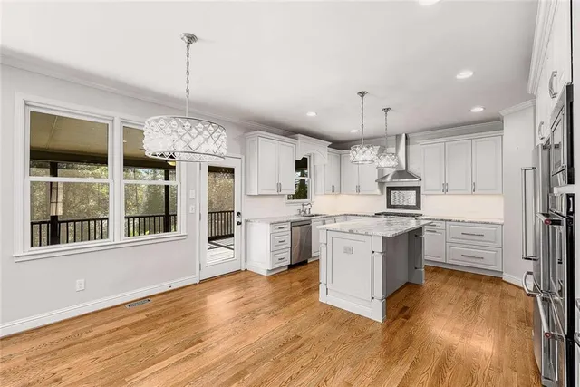 a kitchen with stainless steel appliances granite countertop a refrigerator a oven a sink and white cabinets with wooden floor