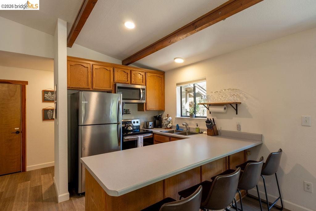 19266 Ferretti Road Groveland, CA 95321 - Photo 5 of 50 Kitchen featuring stainless steel appliances, light countertops, a peninsula, vaulted ceiling with beams, and a kitchen bar