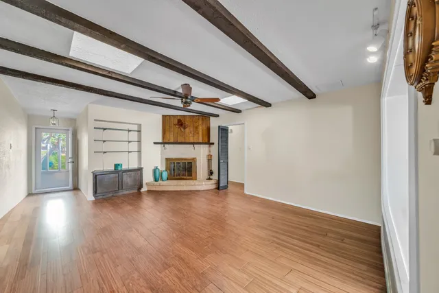 an empty room with wooden floor fire place and windows