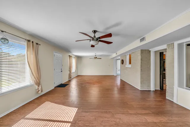 an empty room with wooden floor chandelier fan and windows