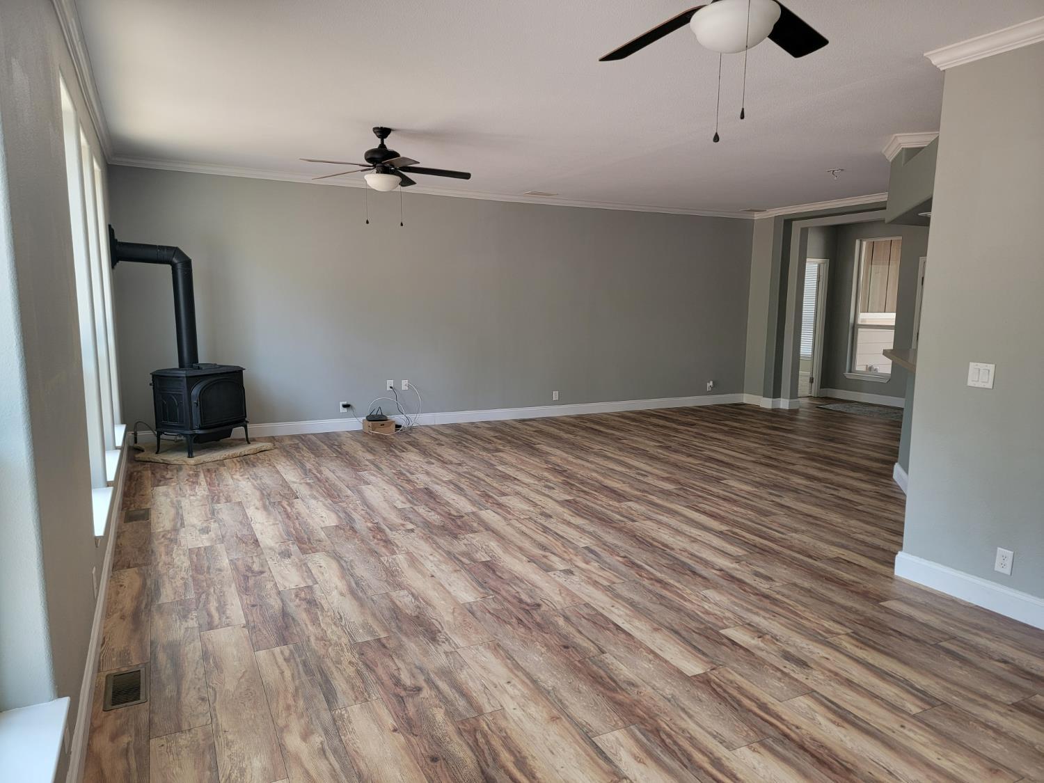 Spacious great room concept featuring wood-finish flooring, a freestanding propane stove, two ceiling fans, crown molding, and neutral wall tones
